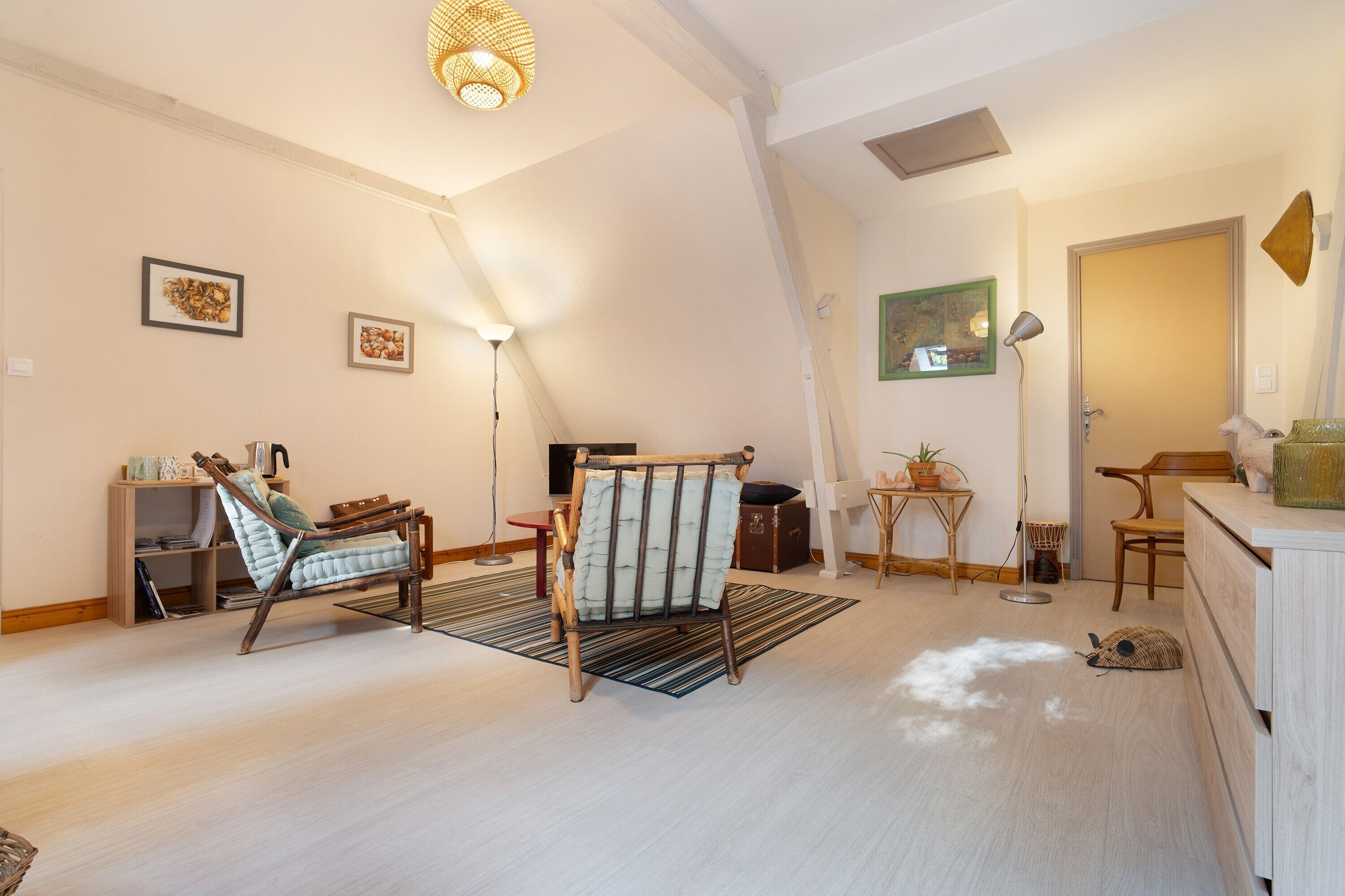 Una habitación amplia con techo inclinado, una cama de madera, una silla, una mesita y una lámpara.