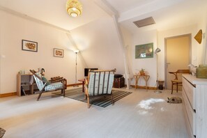 Ein geräumiges Zimmer mit schrägverdeckter Decke, einem hölzernen Bett, einem Sessel, einem kleinen Tisch und einer Lampe.