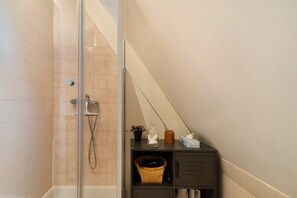 Une salle de bain avec une douche à parois de verre, un porte-serviettes, une étagÚre avec des articles de toilette et un panier en osier.