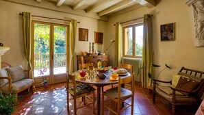 Un comedor con una mesa dispuesta para cuatro personas, rodeada de sillas de madera, un sofá y una ventana con cortinas.