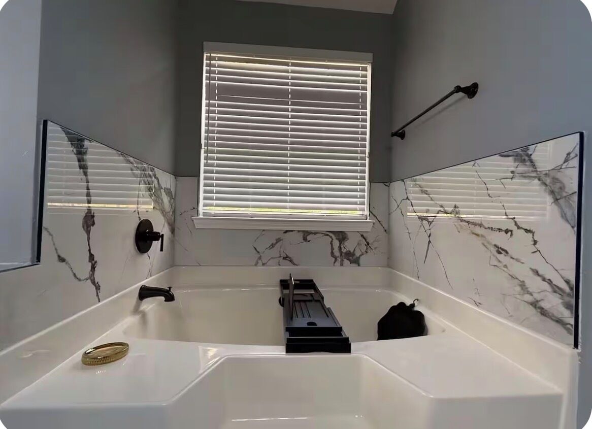 A bathroom with a bathtub, a window with blinds, and marble walls.