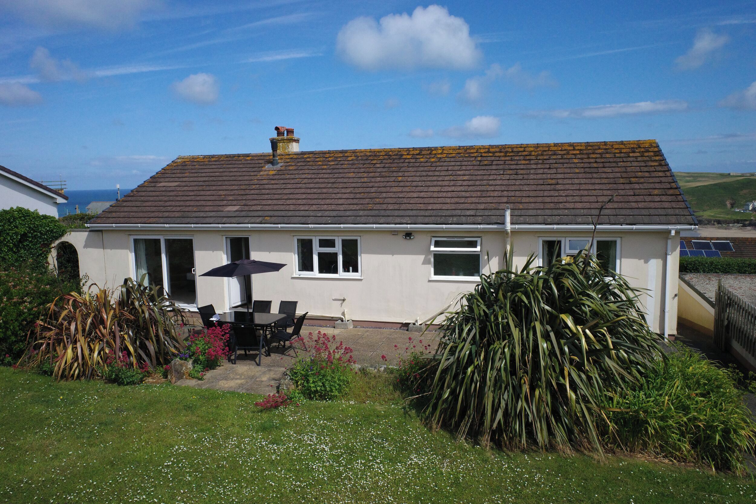 A single-story house with a tiled roof, a patio with a table and chairs, and a garden with various plants.