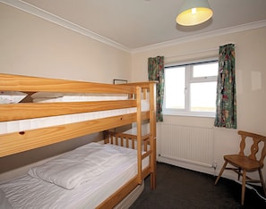 A bunk bed room with a wooden ladder, a chair, a window with curtains, and a radiator. - Badgers Cliff (Wadebridge)