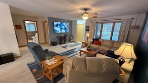 A living room with a sofa, armchair, coffee table, TV, and a ceiling fan. - The Nest, a spacious, secluded pet-friendly retreat! (Barnes)