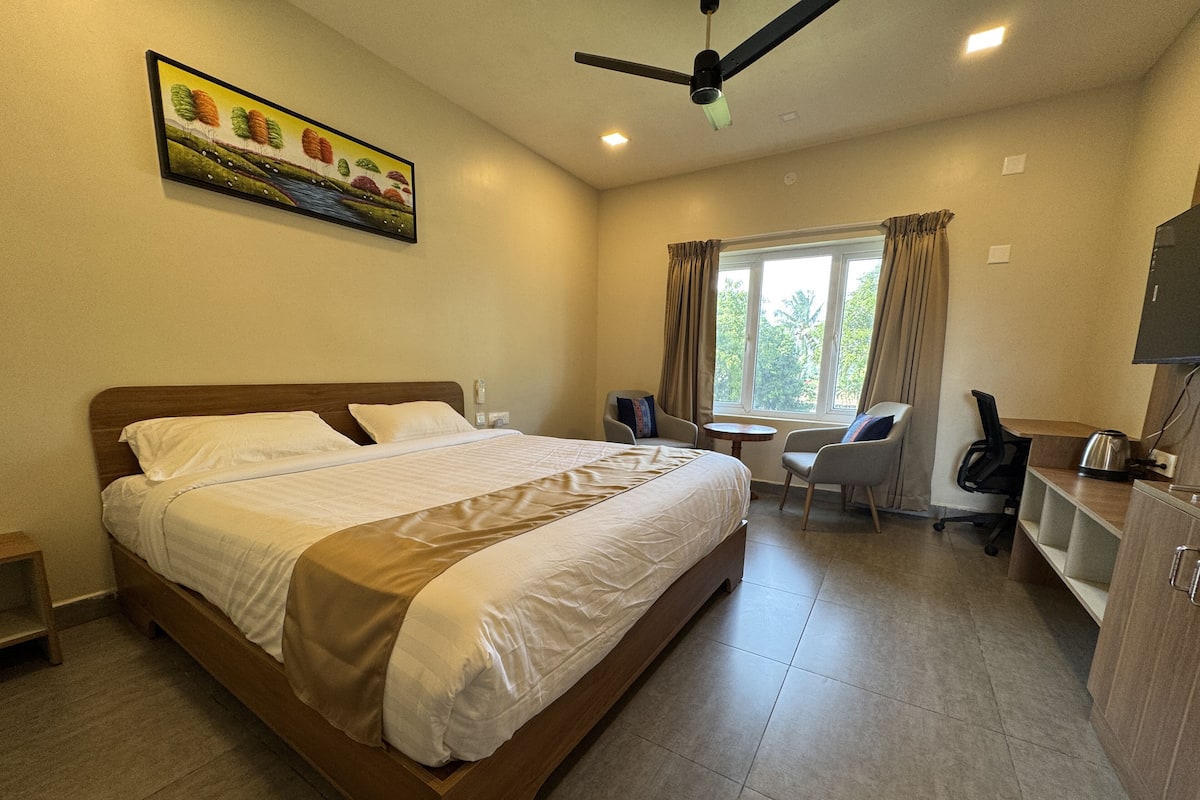 A hotel room with a large bed, a desk, a chair, a television, and a window with curtains.