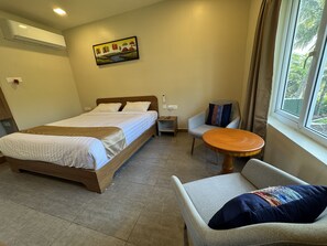 A hotel room with a bed, a chair, a small table, and a window with a view. - Beyond Inn Hotels & Resorts ECR (Cheyyur)