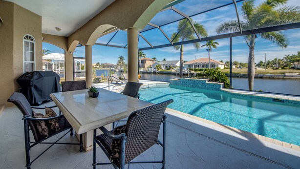 Ein Poolbereich im Freien mit überdachter Terrasse, Sitzgelegenheiten und Blick auf das Wasser.