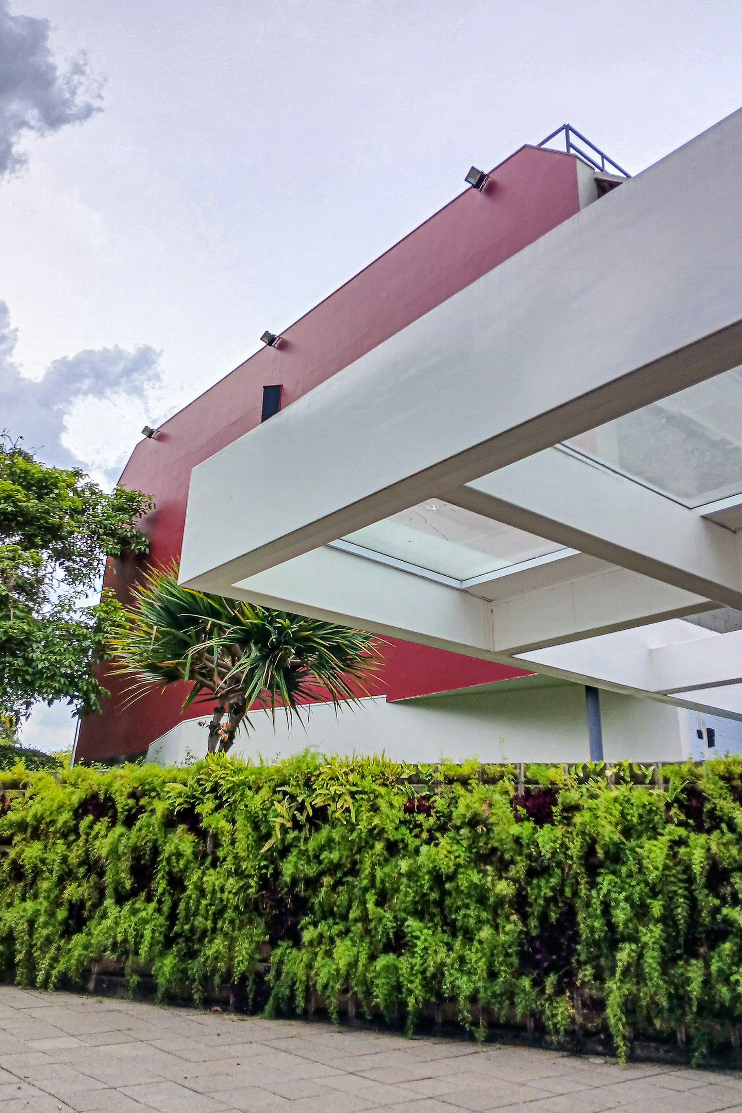 A building with a red and white facade, a covered walkway, and a green hedge in the foreground.