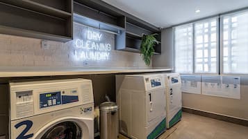 A laundry facility with a neon sign, multiple washing machines, and a trash bin.