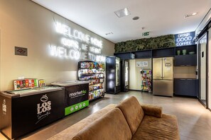 Un vestíbulo moderno con un letrero de 'Welcome', un letrero que dice 'Drink Good Coffee', un quiosco 'Market 4U' y una zona de kitchenette.