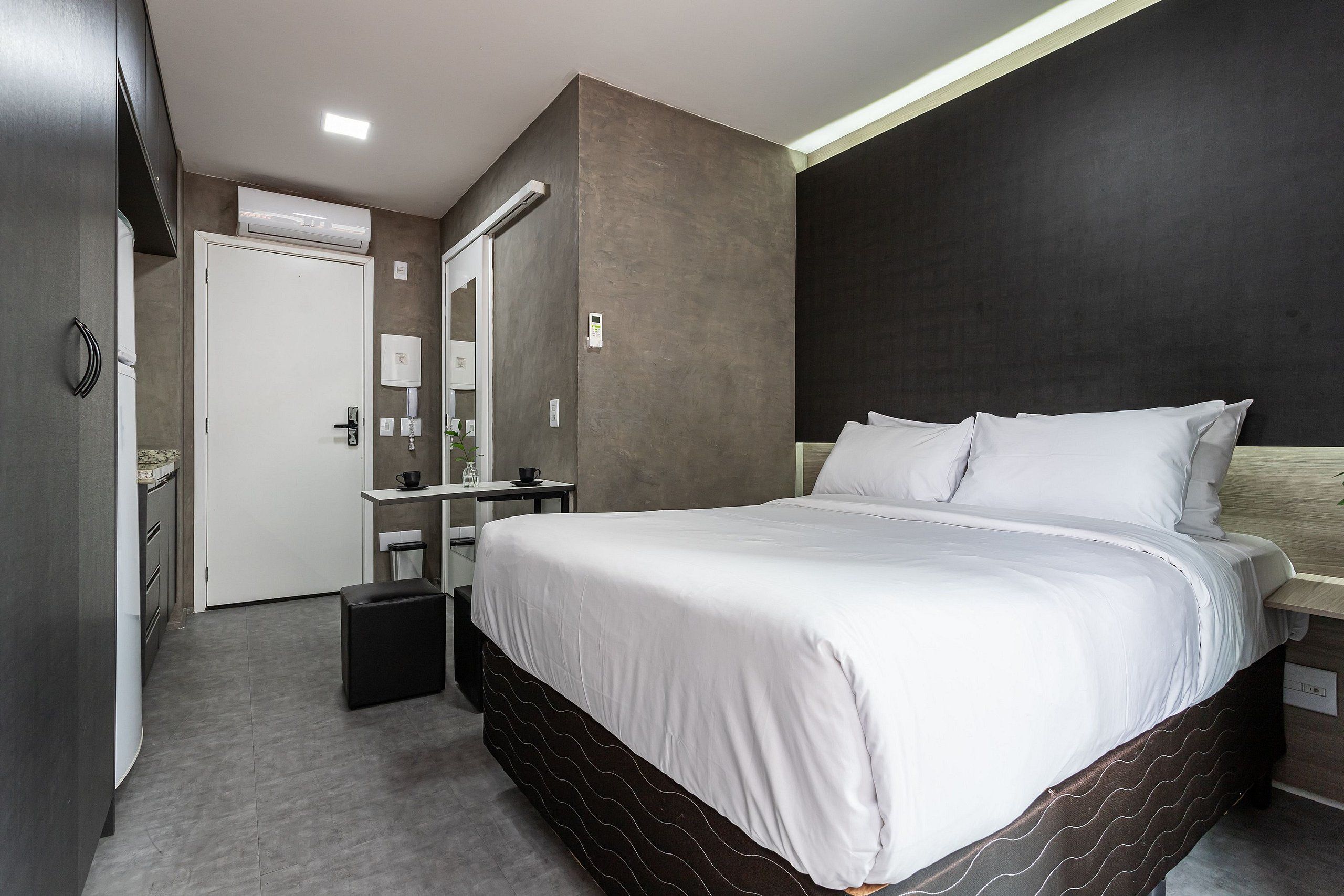 A modern hotel room with a large bed, a bedside table, a mirror, and a wardrobe.