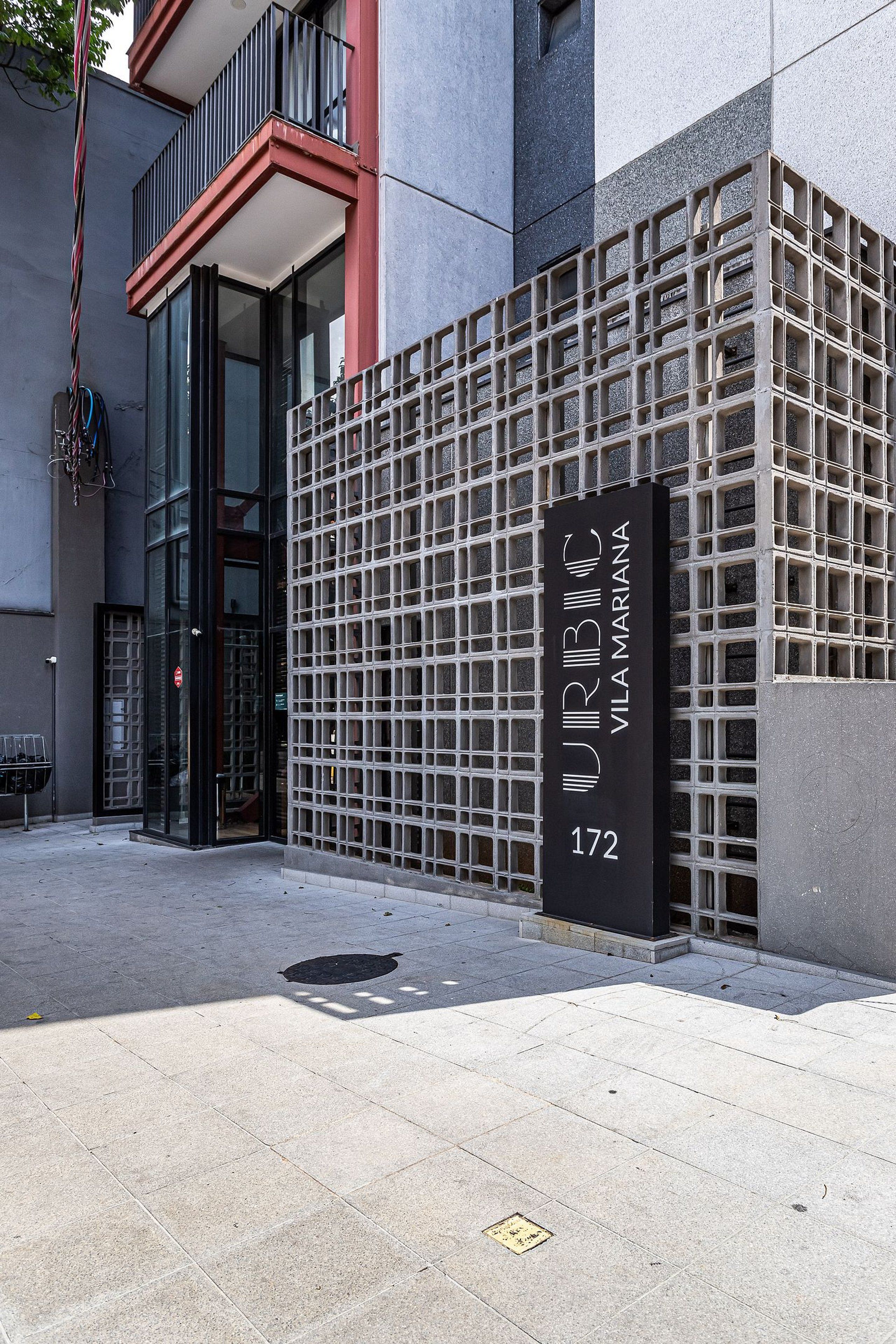 A building facade with a grid-like pattern, a sign with the name 'URBIC VILAMARIANA' and the number '172', and a door with a glass panel.