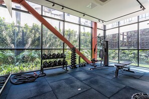 Un gimnasio con amplias ventanas, equipamiento de ejercicio y vistas al exterior a zonas verdes.