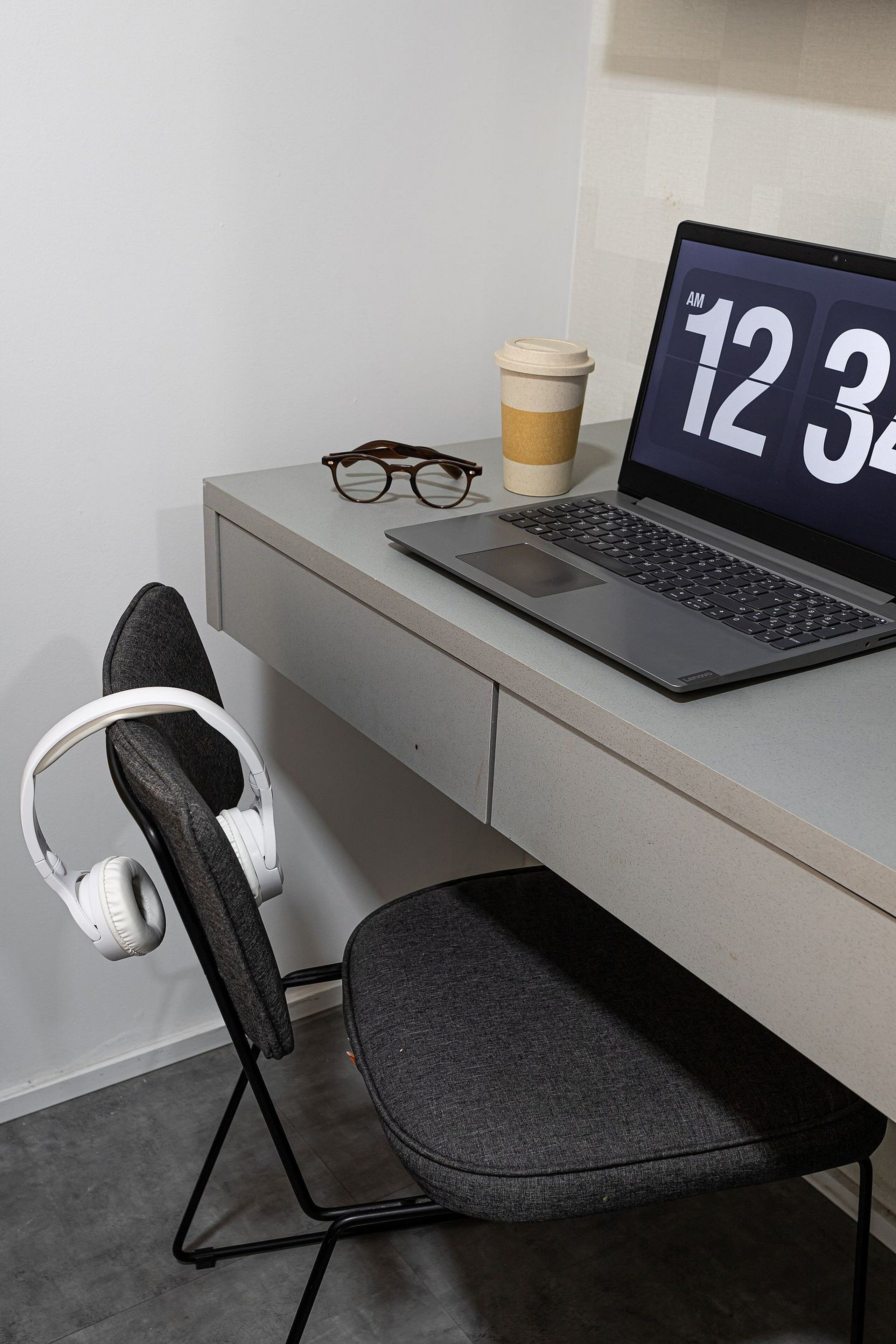 A laptop on a desk with a coffee cup, glasses, and headphones.
