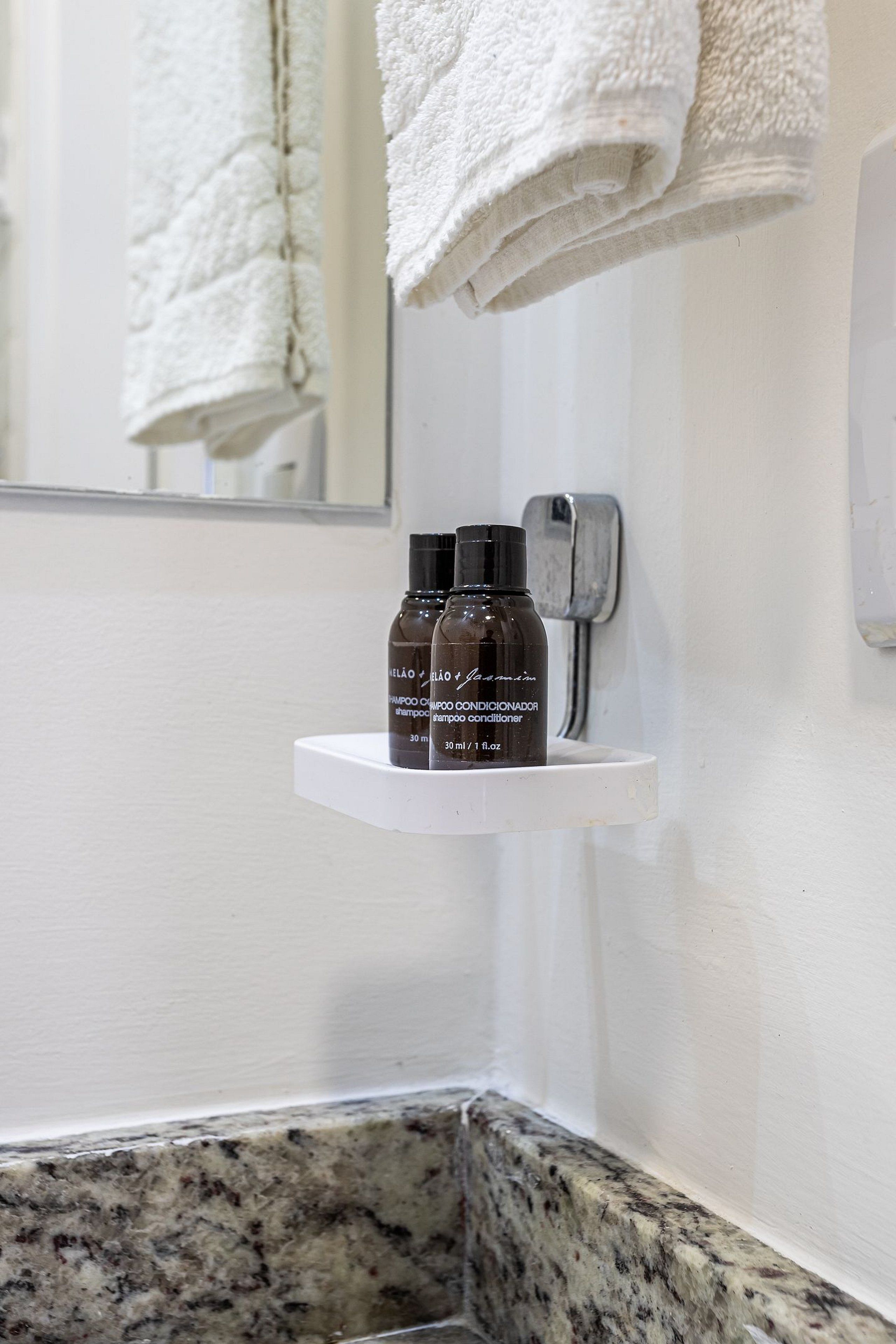 A bathroom with a white sink, a granite countertop, and two bottles of shampoo on a white shelf.