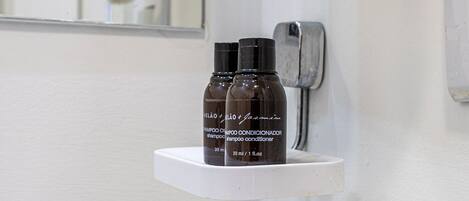 A bathroom with a white sink, a granite countertop, and two bottles of shampoo on a white shelf.