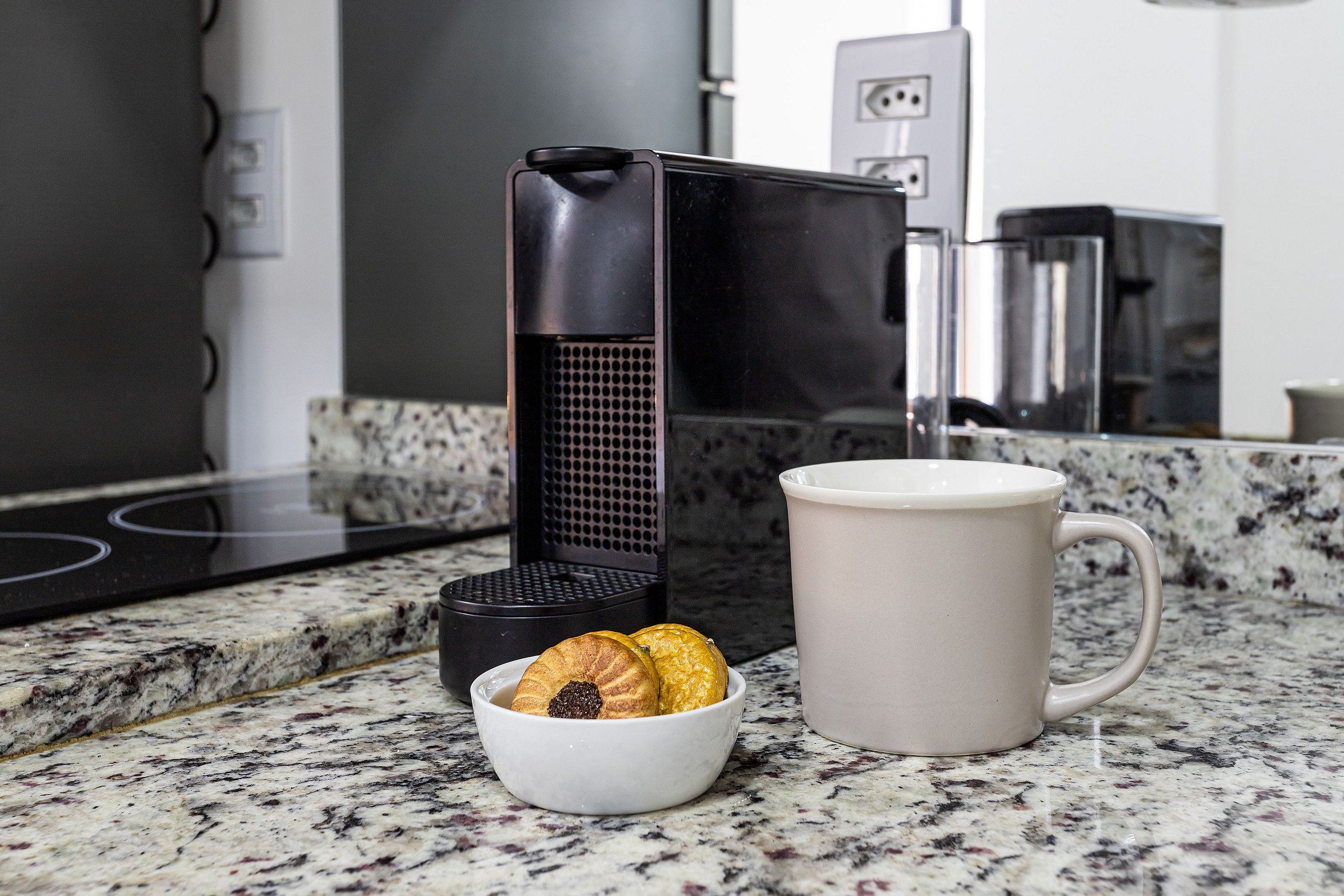 Eine Küche mit Kaffeemaschine, einer Tasse und einer Schüssel Kekse auf einer Granitarbeitsplatte.