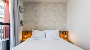 A neatly made bed with white linens, two bedside lamps, a wooden headboard, and a wall with a geometric pattern. - Urbic Vila Mariana by Viva - Prédio com academia e coworking a passos da ESPM, Belas Artes e Metrô (São Paulo)