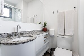 Un baño con lavabo blanco, espejo, ducha e inodoro.