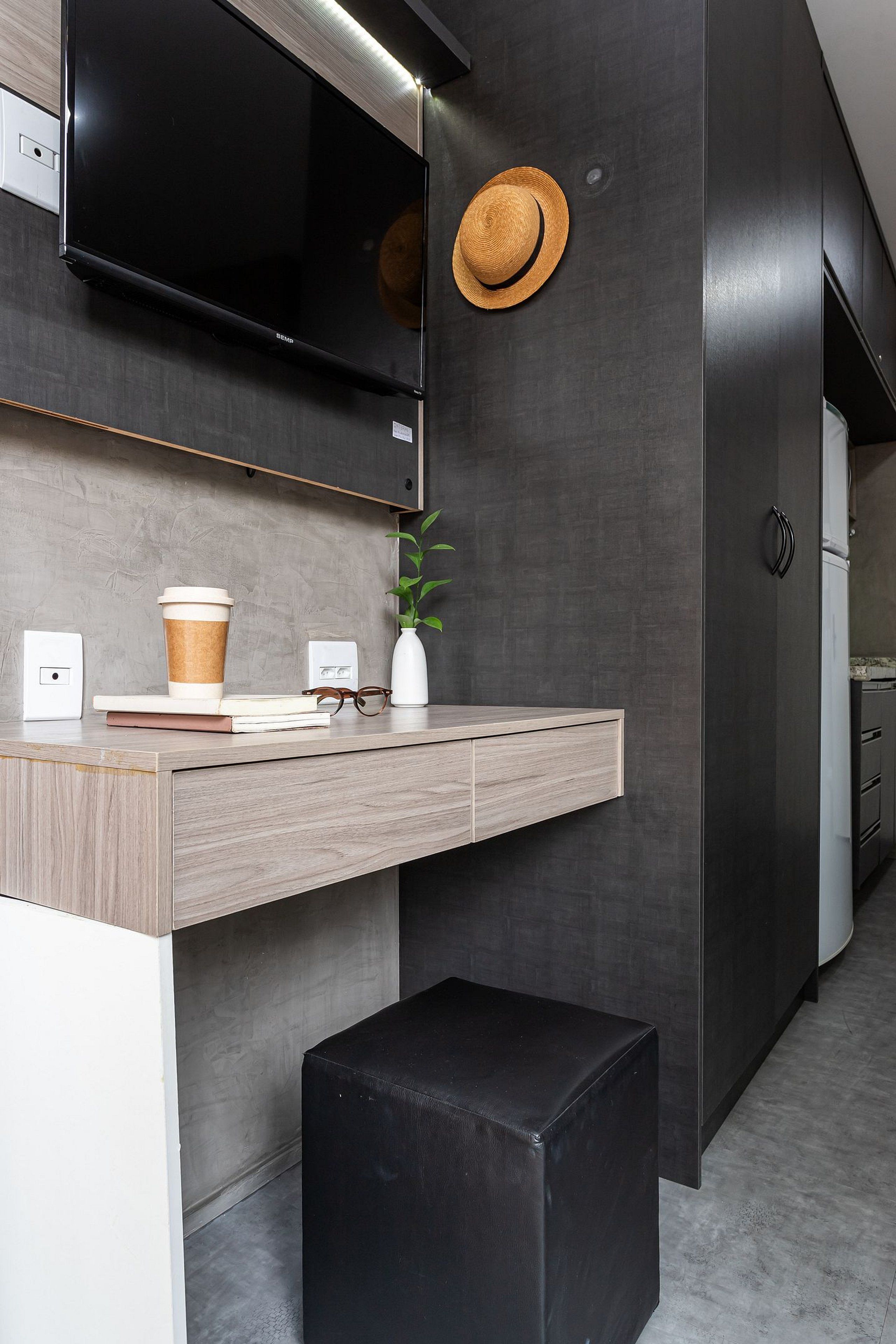 A modern kitchen with a built-in oven, a coffee cup, a vase with a plant, and a black ottoman.