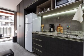 A compact kitchenette with a refrigerator, microwave, coffee maker, and a sink. - Urbic Vila Mariana by Viva - Prédio com academia e coworking a passos da ESPM, Belas Artes e Metrô (São Paulo)