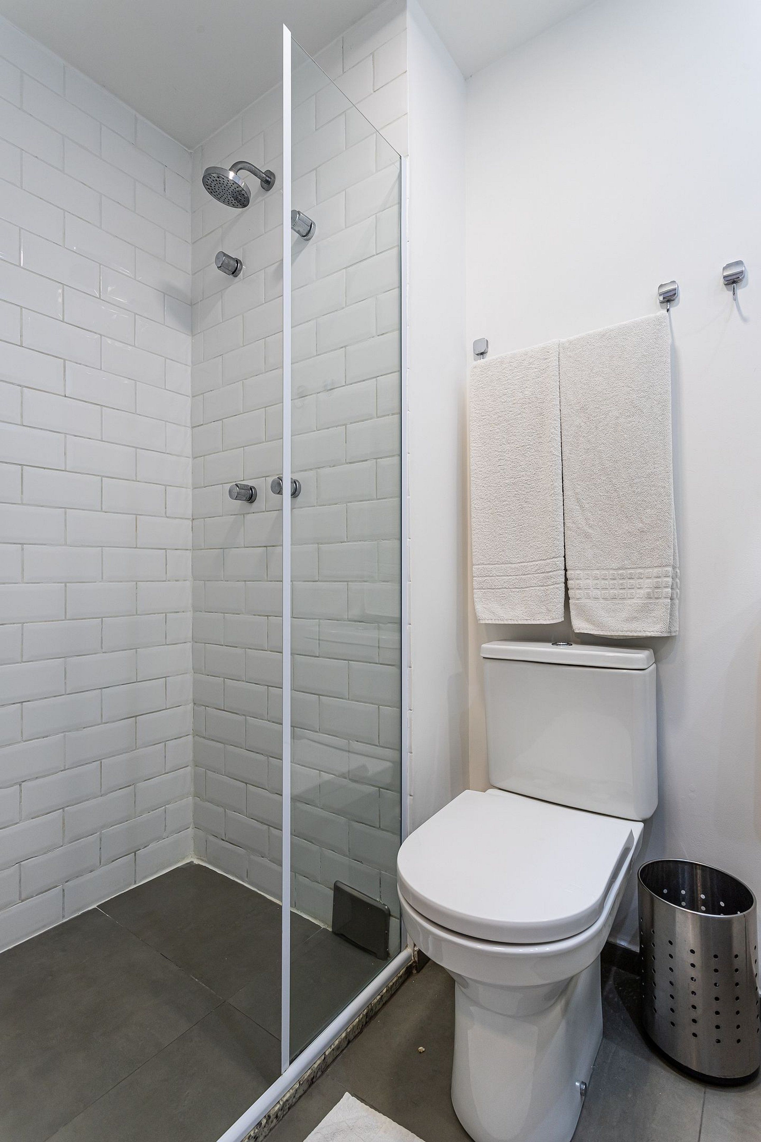 Ein Badezimmer mit weißen Fliesen, einer Glasdusche, einer Toilette und zwei Handtüchern, die an der Wand hängen.