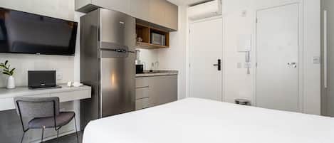 A modern hotel room with a bed, a desk with a laptop, a chair, a refrigerator, a microwave, and a television.