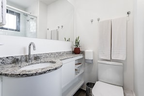 Un baño con lavabo blanco, espejo, ducha e inodoro.