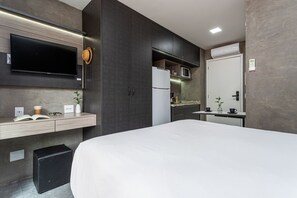 Una habitación de hotel moderna con una cama grande, un televisor de pantalla plana montado en la pared, un pequeño espacio con microondas y un baño independiente con inodoro y lavamanos.