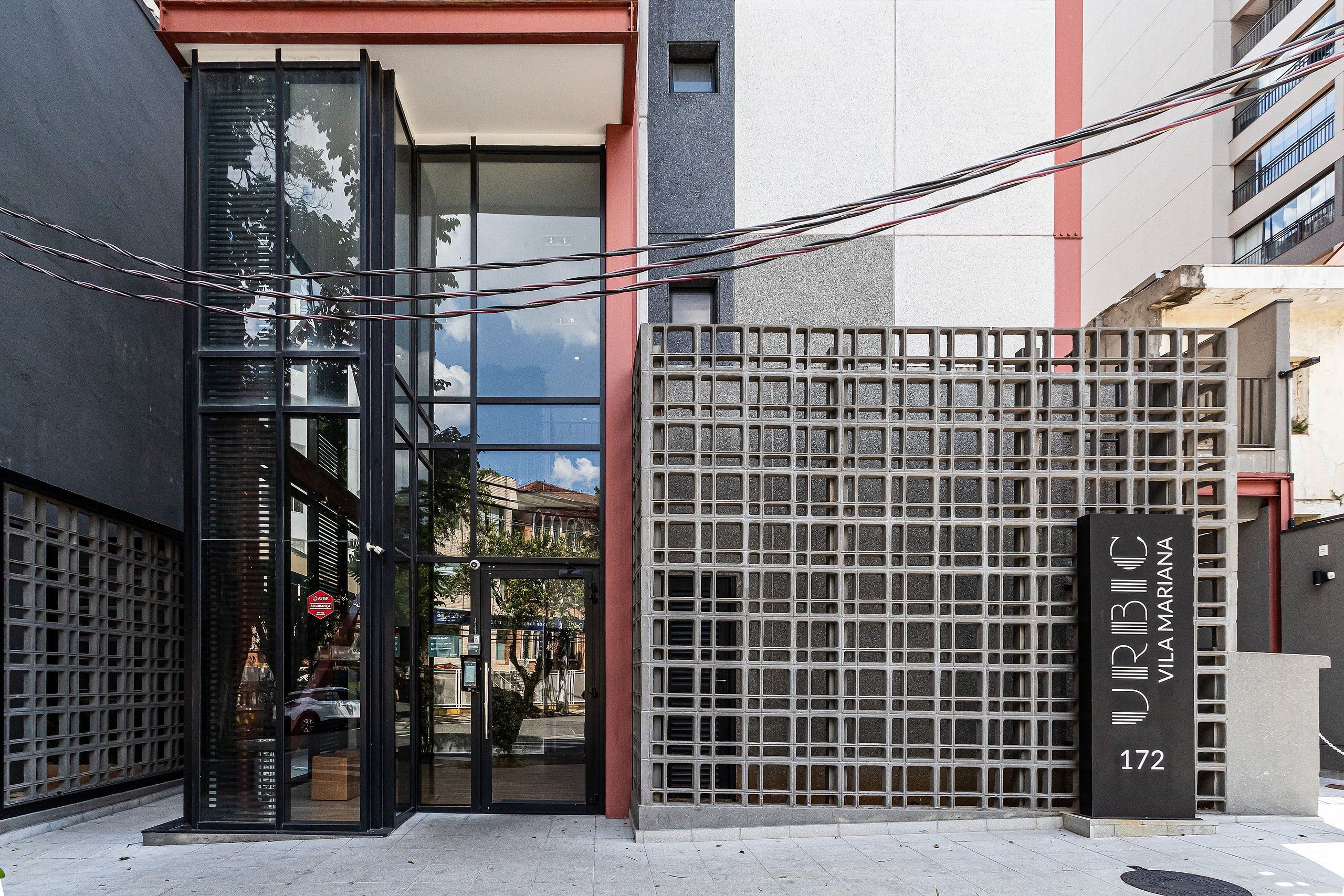 Un bâtiment moderne avec une entrée en verre, un portail en métal et une enseigne indiquant l’adresse « VILA MARINA 172 ».