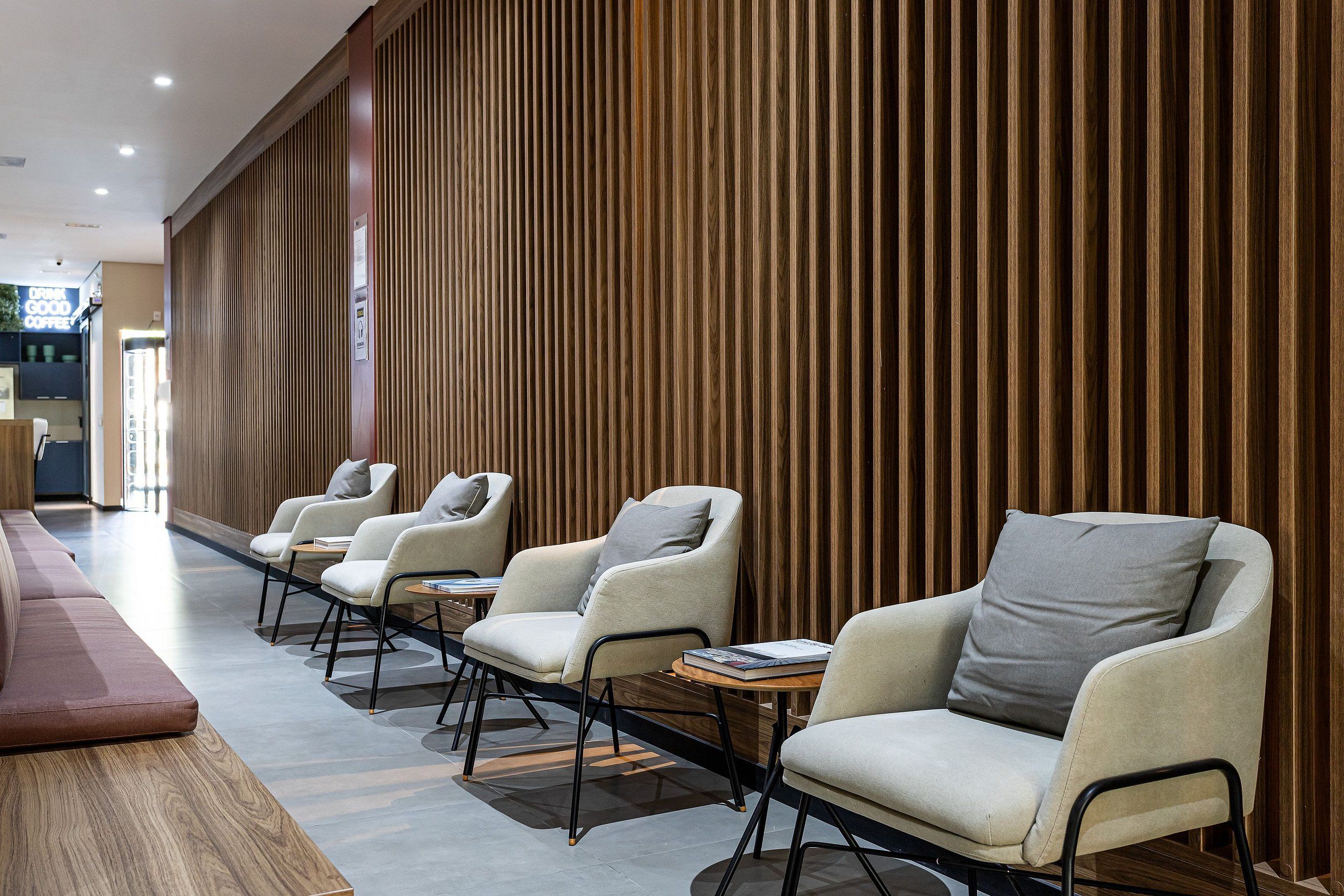 A modern hotel lobby with a long wooden wall, a red sofa, and three beige armchairs with books.