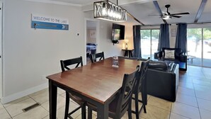 Un comedor con una mesa y sillas de madera, un letrero que dice "Welcome to the Lake", un ventilador de techo y vistas al exterior.