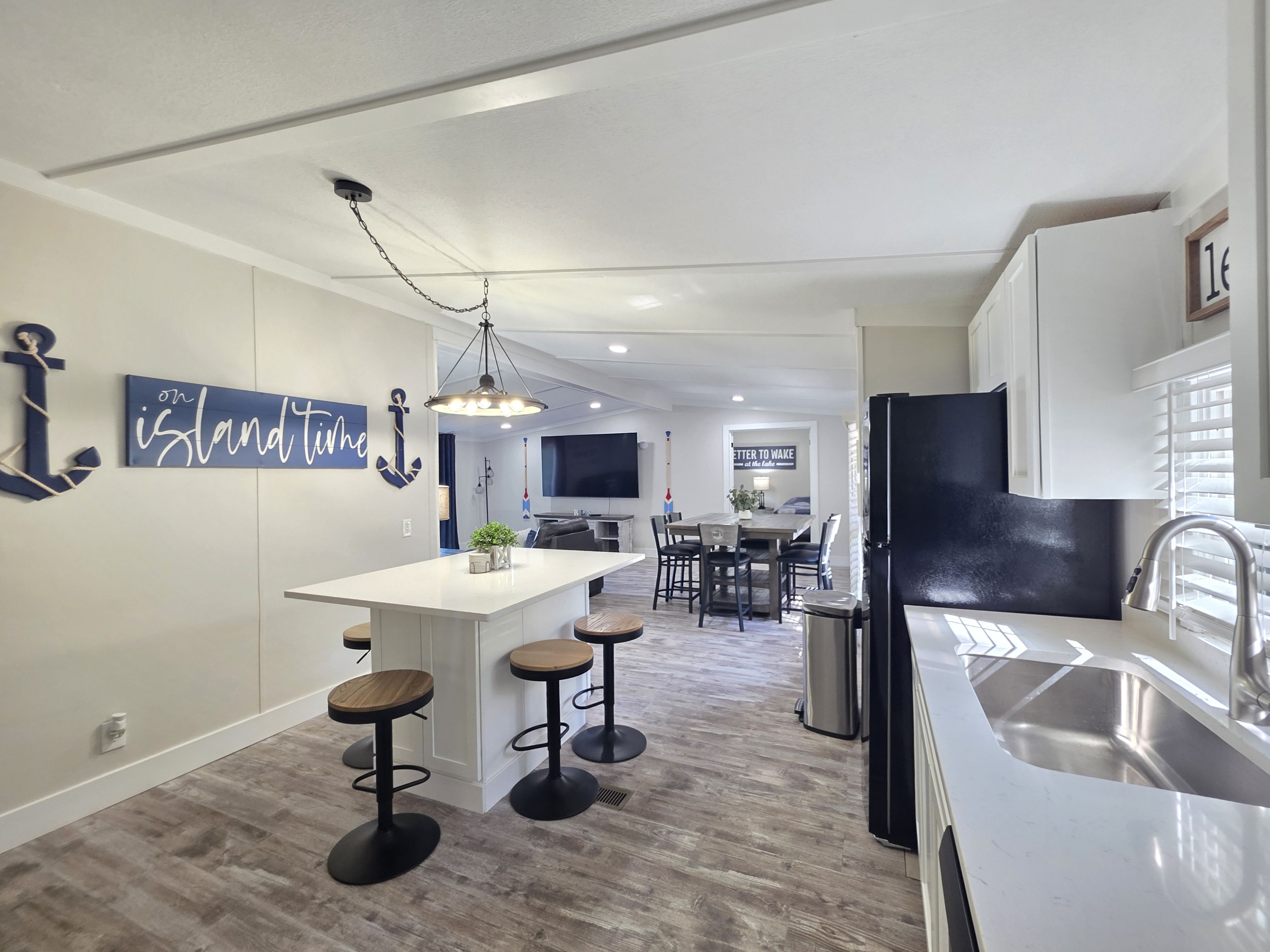 A modern kitchen with a central island, bar stools, a stainless steel sink, and a dining area with a TV.
