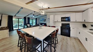A modern kitchen with white cabinets, a large island with bar stools, and a microwave. - Brand-New Beauty—Relax & Recharge | 8 ppl | IC68 (Put-in-Bay)