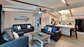 A modern living room with two black leather sofas, a wooden coffee table, and a kitchen in the background. - Brand-New Beauty—Relax & Recharge | 8 ppl | IC68 (Put-in-Bay)