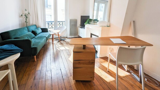 Een modern appartement met een houten vloer, een groene bank, een eettafel met stoelen, een televisie en een balkon met uitzicht.