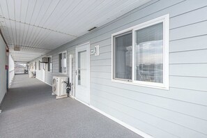 A corridor with a covered walkway, air conditioning units, and a row of rooms with windows and doors. - Walk-to-Beach Condo with a Pool (Ocean City)