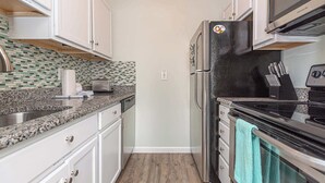Una cocina compacta con armarios blancos, un refrigerador negro, un microondas y un tostador.