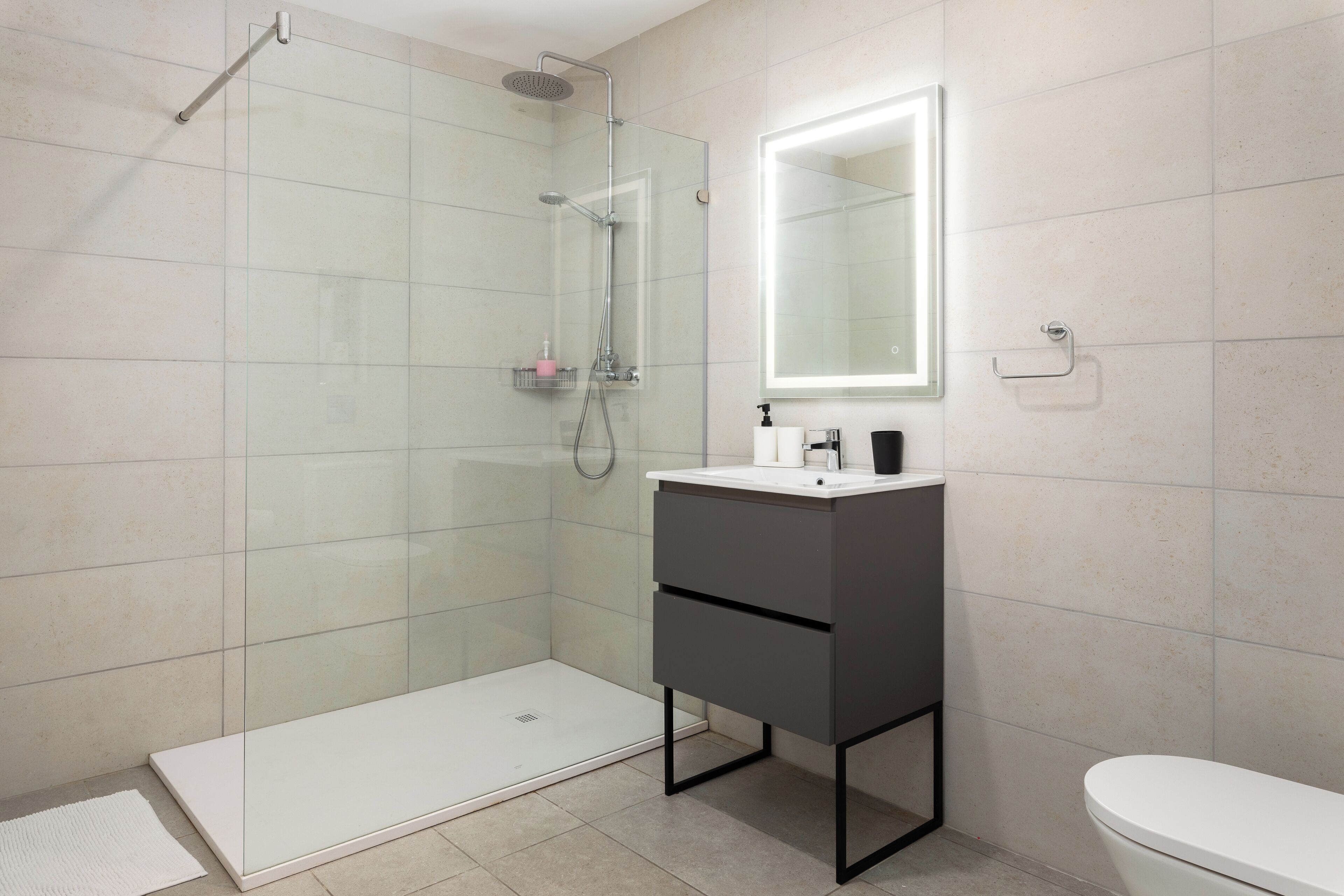 Un baño moderno con ducha de vidrio, un lavamanos blanco y un espejo encima, y un inodoro.