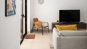 En moderne stue med sofa, fjernsyn, stol og pendel.