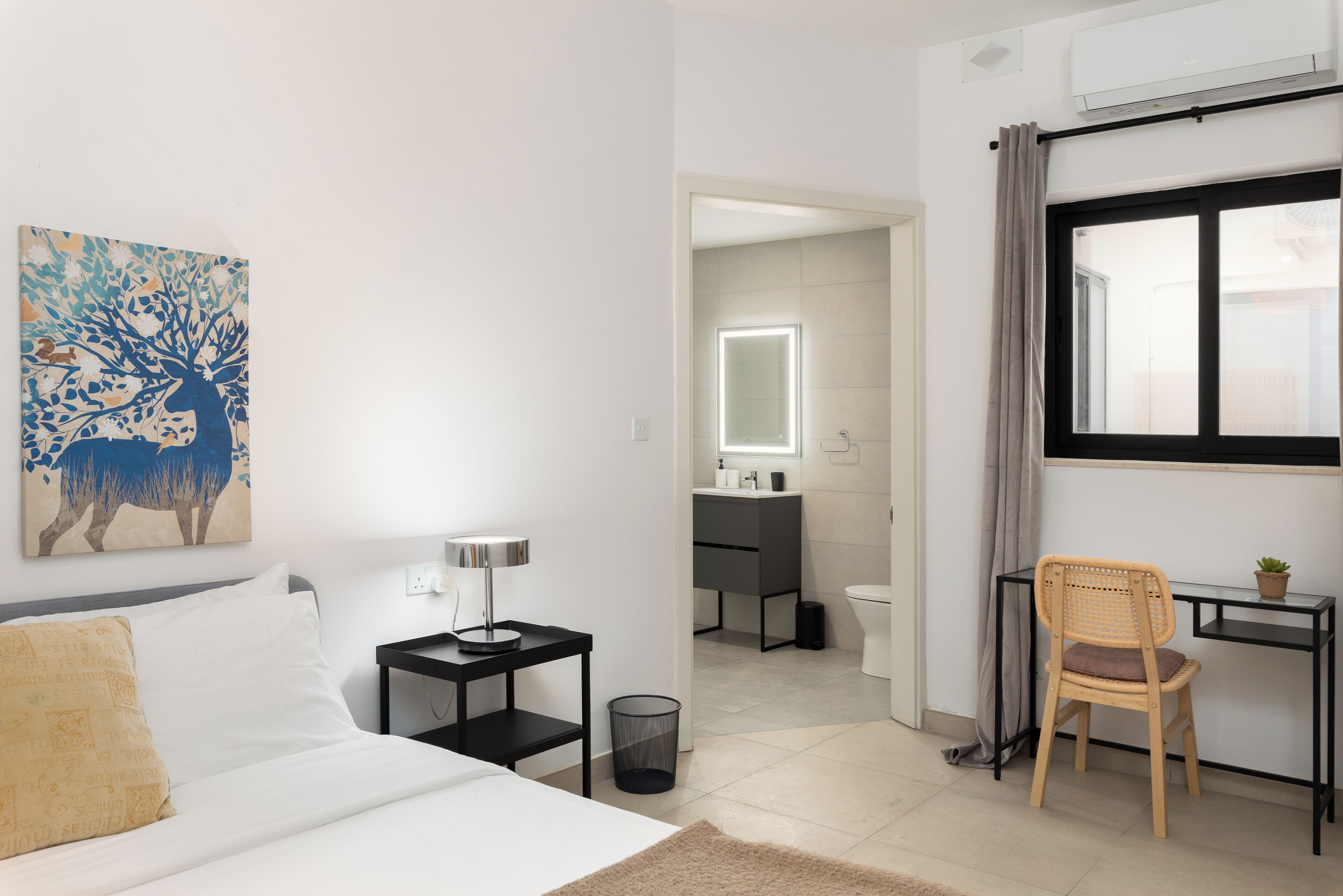 Un dormitorio con cama, mesita de noche, lámpara, silla y un cuadro en la pared.