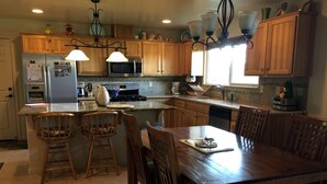 A kitchen with wooden cabinets, a dining table, bar stools, and a stove. - Luxury Cabin Rental with a Fire Pit in Coulterville, California (Yosemite)