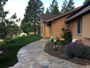 A house with a stone pathway leading to a wooden door, surrounded by a well-maintained garden with various plants and flowers. - Luxury Cabin Rental with a Fire Pit in Coulterville, California (Yosemite)