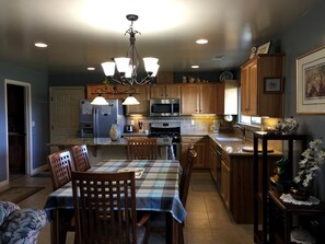 Una cocina con armarios de madera, una mesa de comedor con sillas, una araña y un microondas.