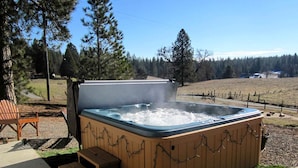 An outdoor hot tub with steps, surrounded by a wooden deck and a stone pathway.