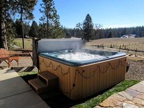 Un bain à remous extérieur avec des marches, entouré d’une terrasse en bois et d’un chemin en pierre.