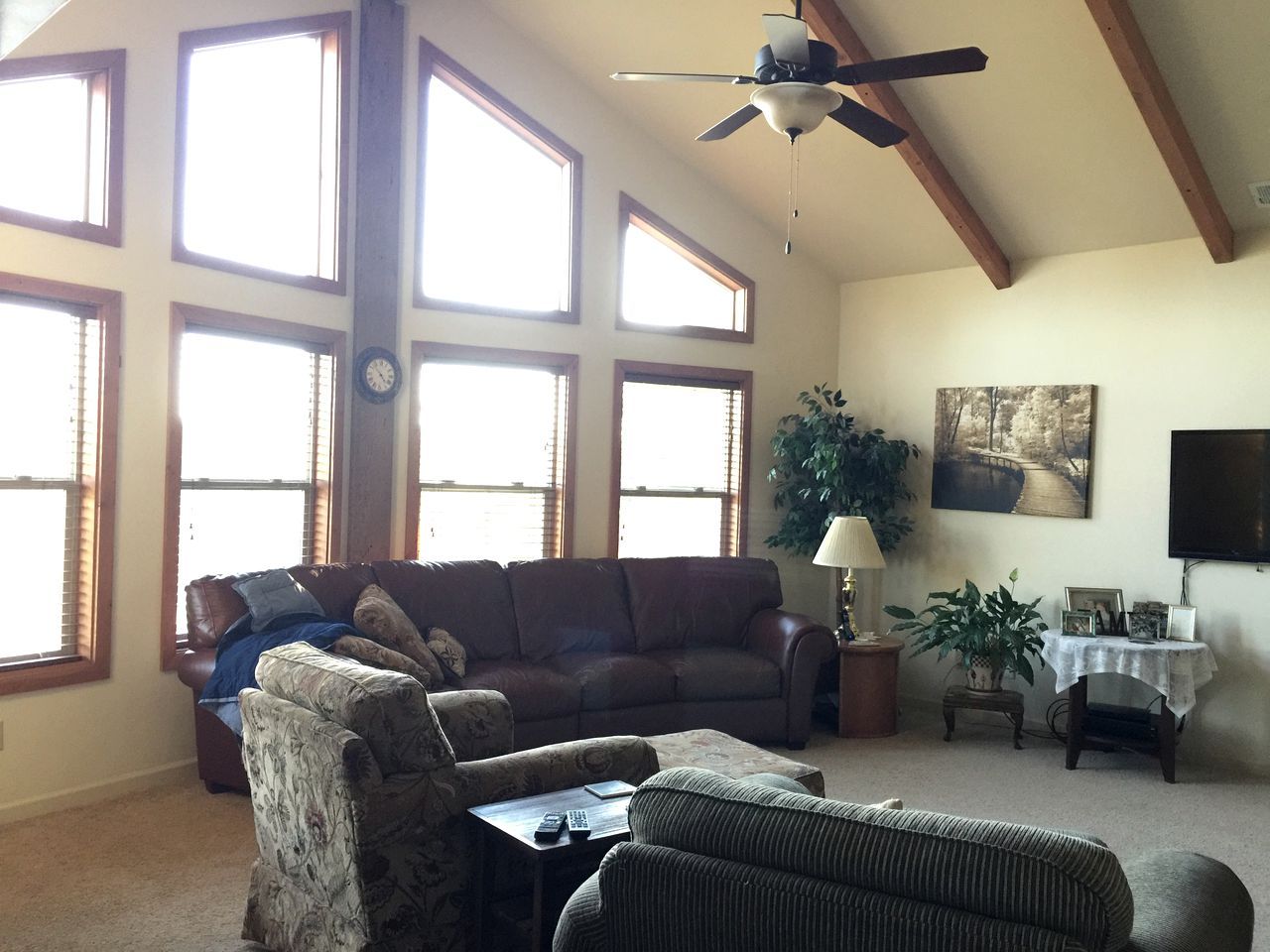 A spacious living room with a large window, a ceiling fan, and a television.