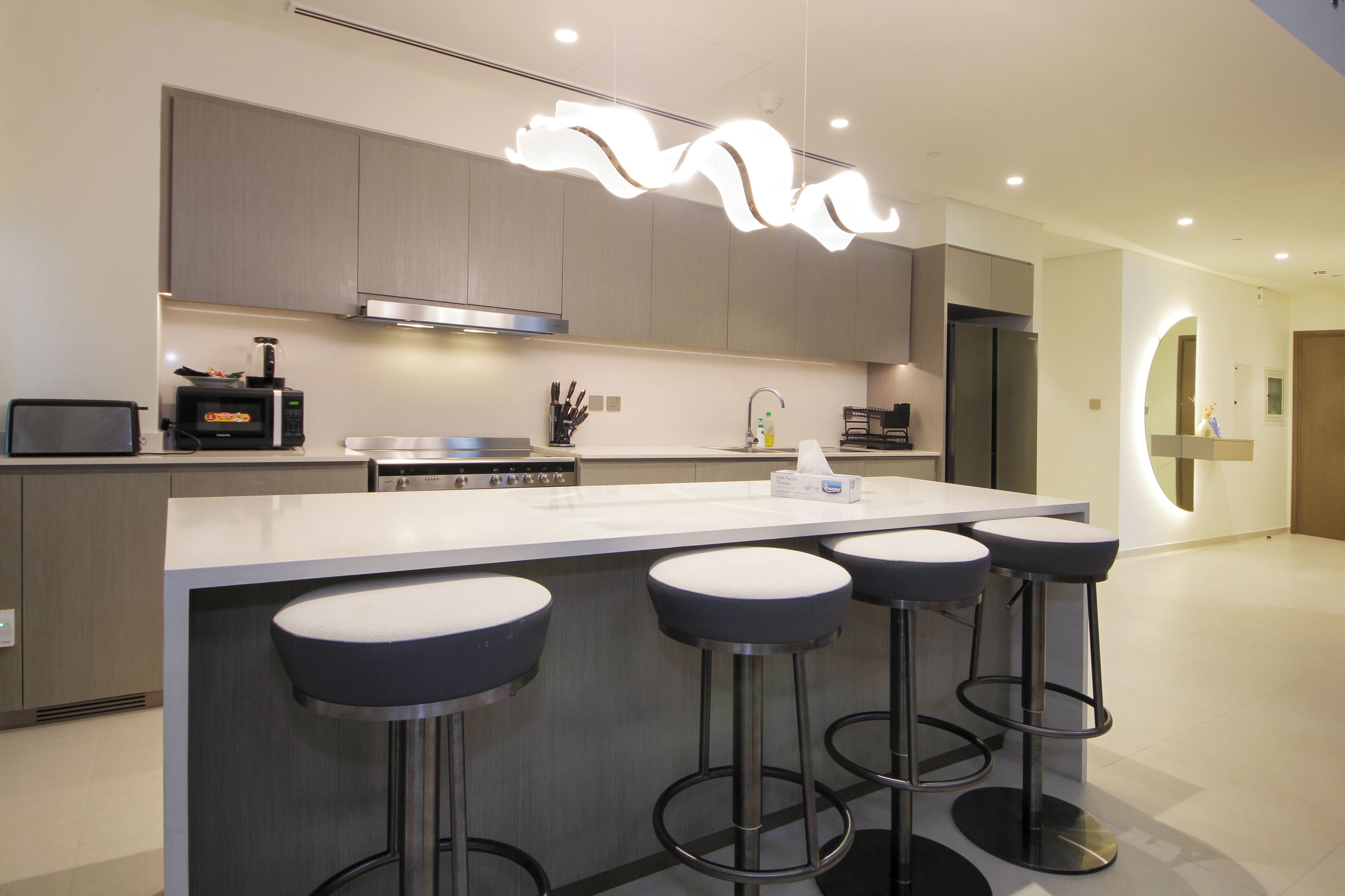 A modern kitchen with a central island, bar stools, stainless steel appliances, and a unique ceiling light fixture.