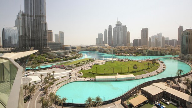 A cityscape with a prominent curved water feature, modern high-rise buildings, and a well-maintained green space. - 3BHK Sea View Near Palm Jumeirah Avani  (Dubai)