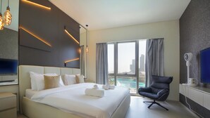 A modern hotel room with a large bed, a flat-screen TV, a desk, and a view of the city. - 3BHK Sea View Near Palm Jumeirah Avani  (Dubai)